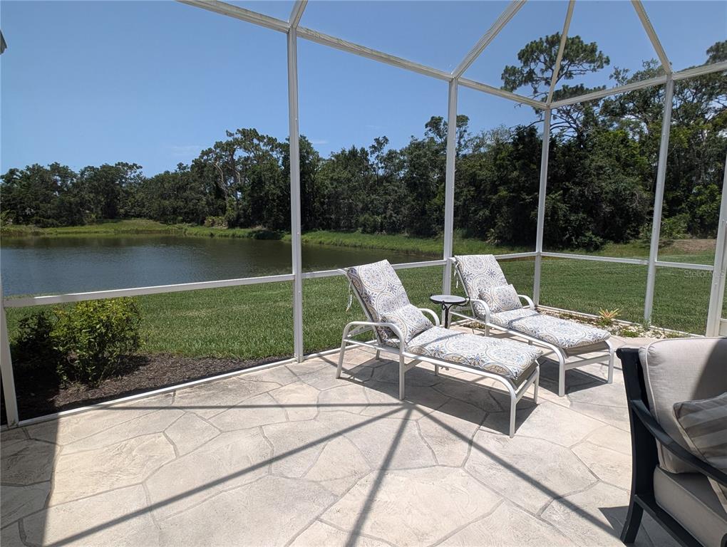 A screened-in patio features stone flooring, two lounge chairs, and a view of a pond — 4406 REFLECTIONS PARKWAY, SARASOTA, FL