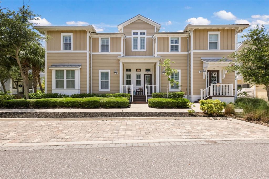 A two-story tan house with white trim and two front porches sits behind a paved street — 258 SAPPHIRE LAKE DRIVE UNIT 202, BRADENTON, FL