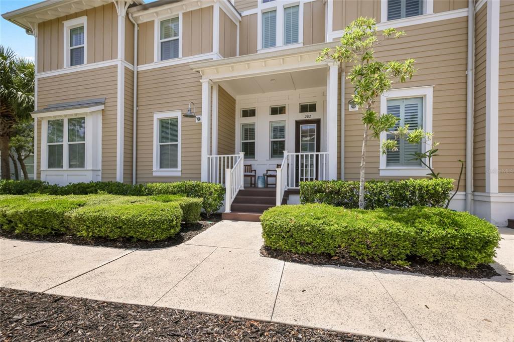 A tan two-story building features a covered front porch with steps and manicured hedges — 258 SAPPHIRE LAKE DRIVE UNIT 202, BRADENTON, FL