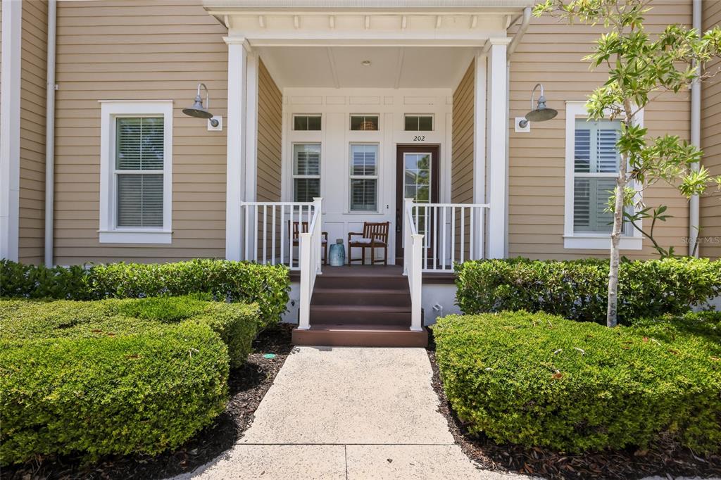 A tan house exterior features a covered front porch with steps and a white railing — 258 SAPPHIRE LAKE DRIVE UNIT 202, BRADENTON, FL