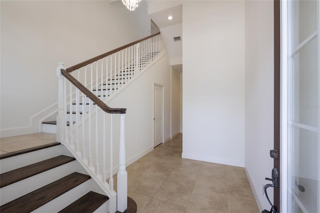 An entryway features a tiled floor, a white staircase with dark wood treads, and a chandelier — 258 SAPPHIRE LAKE DRIVE UNIT 202, BRADENTON, FL
