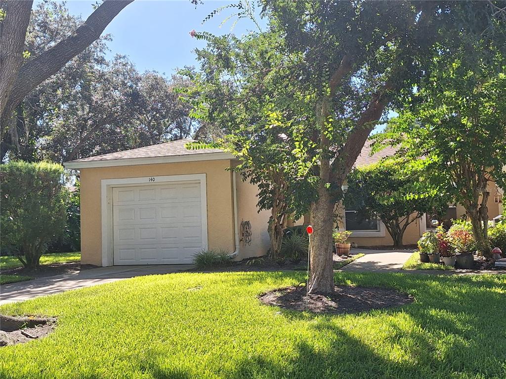 A single-story house with a tan exterior, a white garage door, and a front lawn — 140 TURNBULL VILLAS CIRCLE, NEW SMYRNA BEACH, FL