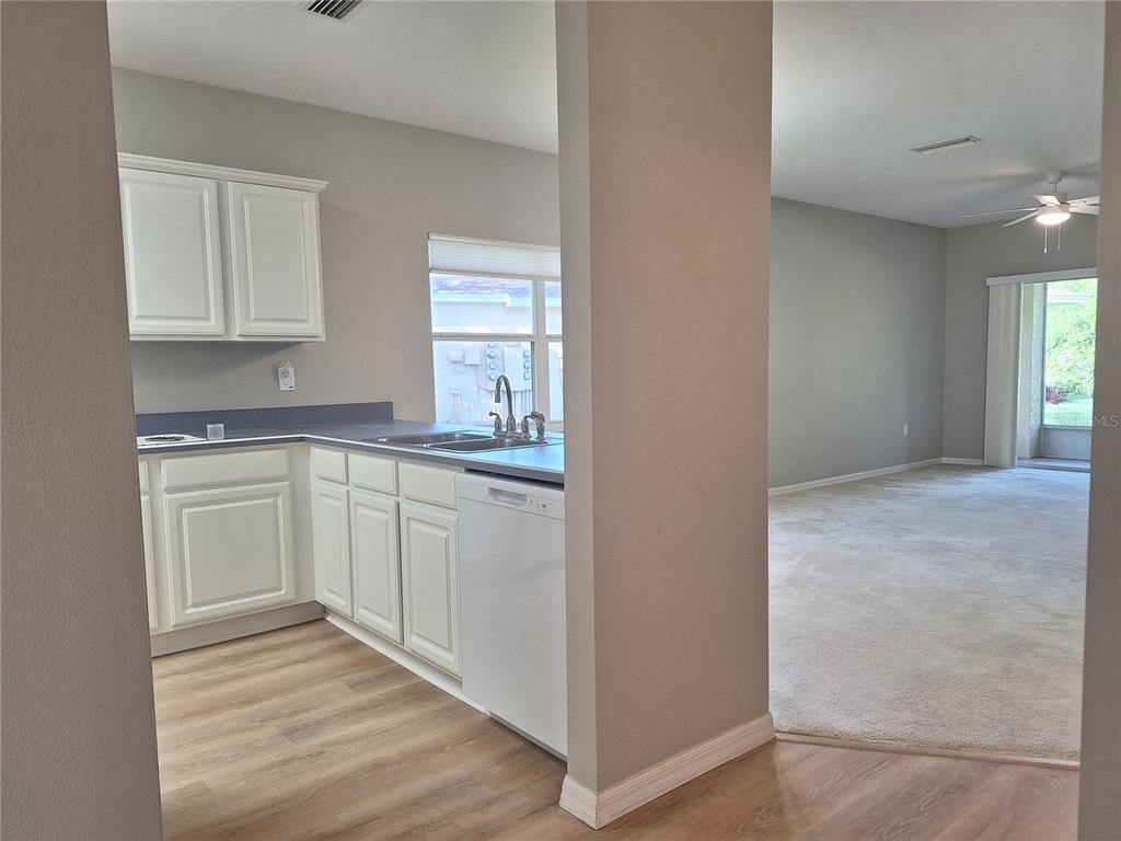 A kitchen with white cabinets and a dishwasher opens into a carpeted living area — 140 TURNBULL VILLAS CIRCLE, NEW SMYRNA BEACH, FL