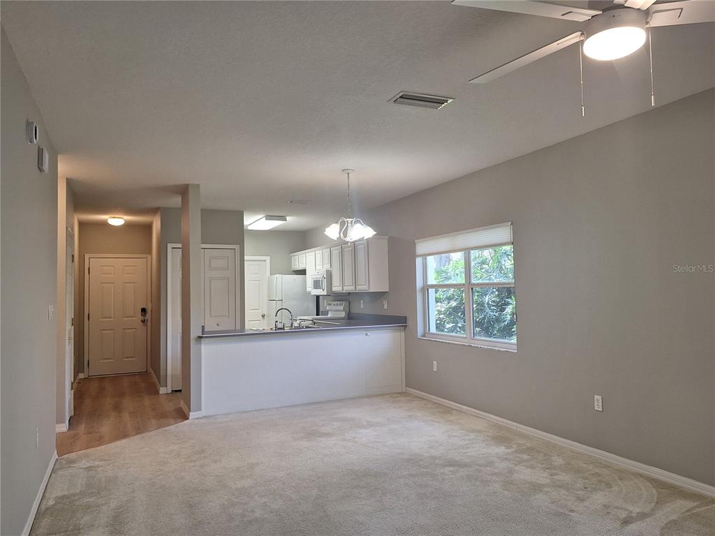 A living room with beige carpet opens to a kitchen with white cabinets and counters — 140 TURNBULL VILLAS CIRCLE, NEW SMYRNA BEACH, FL