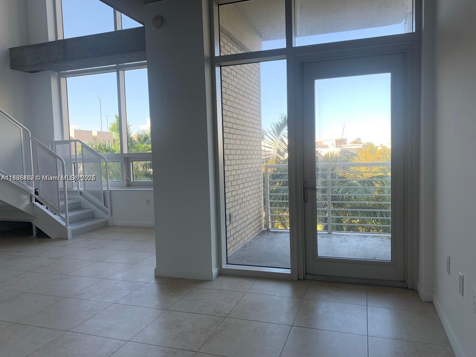 A bright room features light tile floors, a staircase, and a glass door to a balcony — 3250 NE 1st Ave # 303, Miami FL 33137, MIAMI, FL