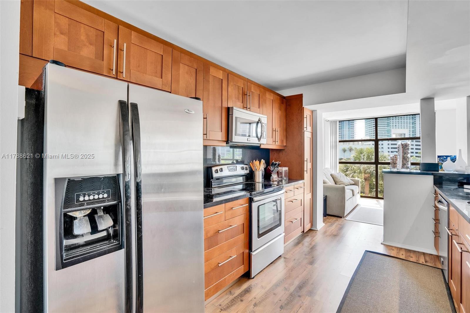 A kitchen features wood cabinets, stainless steel appliances, and dark countertops with an adjacent living area — 600 Parkview Dr, Hallandale Beach FL 33009, HALLANDALE BEACH, FL