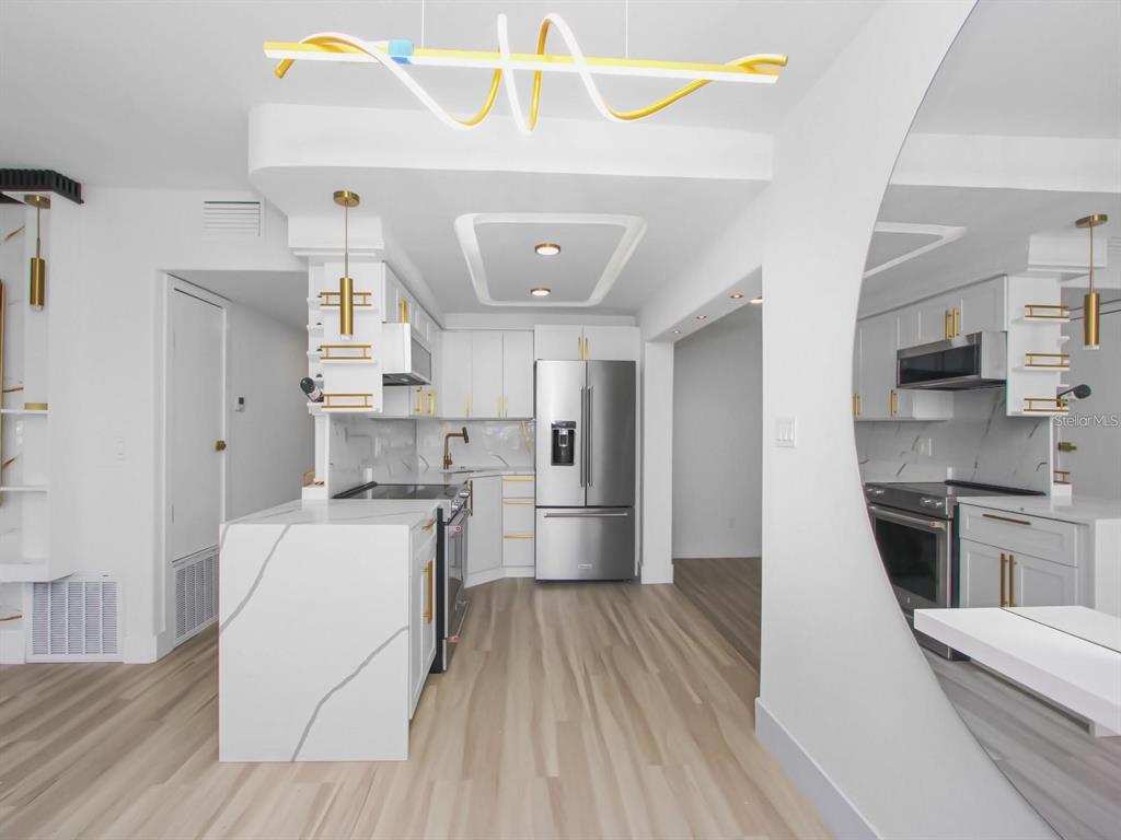 A modern kitchen features white cabinetry, marble-patterned countertops, stainless steel appliances, and a unique chandelier — 4201 PARK LAKE STREET, ORLANDO, FL