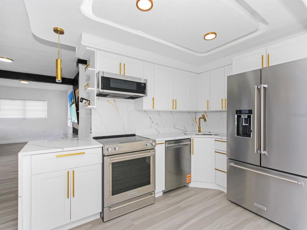 A modern kitchen features white cabinets, gold hardware, stainless steel appliances, and marble-patterned backsplashes — 4201 PARK LAKE STREET, ORLANDO, FL