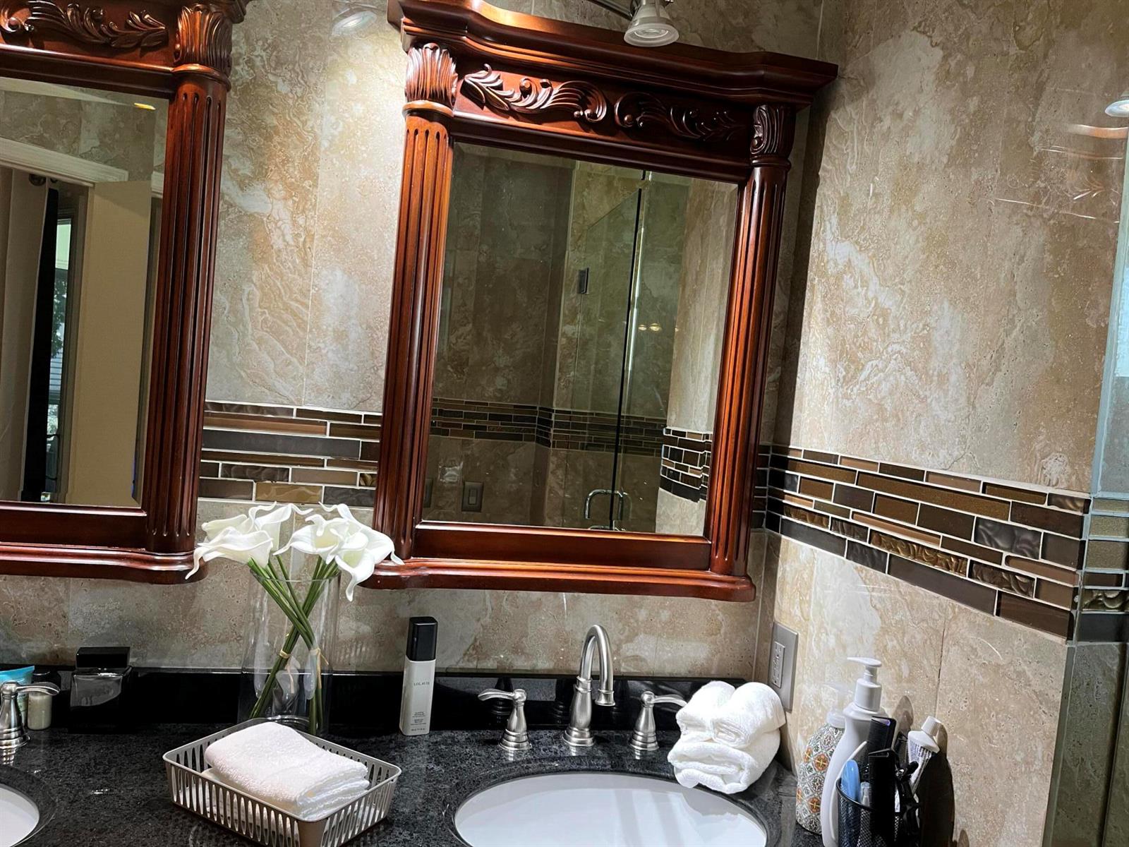A bathroom vanity features a dark wood mirror, granite countertop, and decorative tile backsplash — 6549 Via Regina # 6549, Boca Raton FL 33433, BOCA RATON, FL
