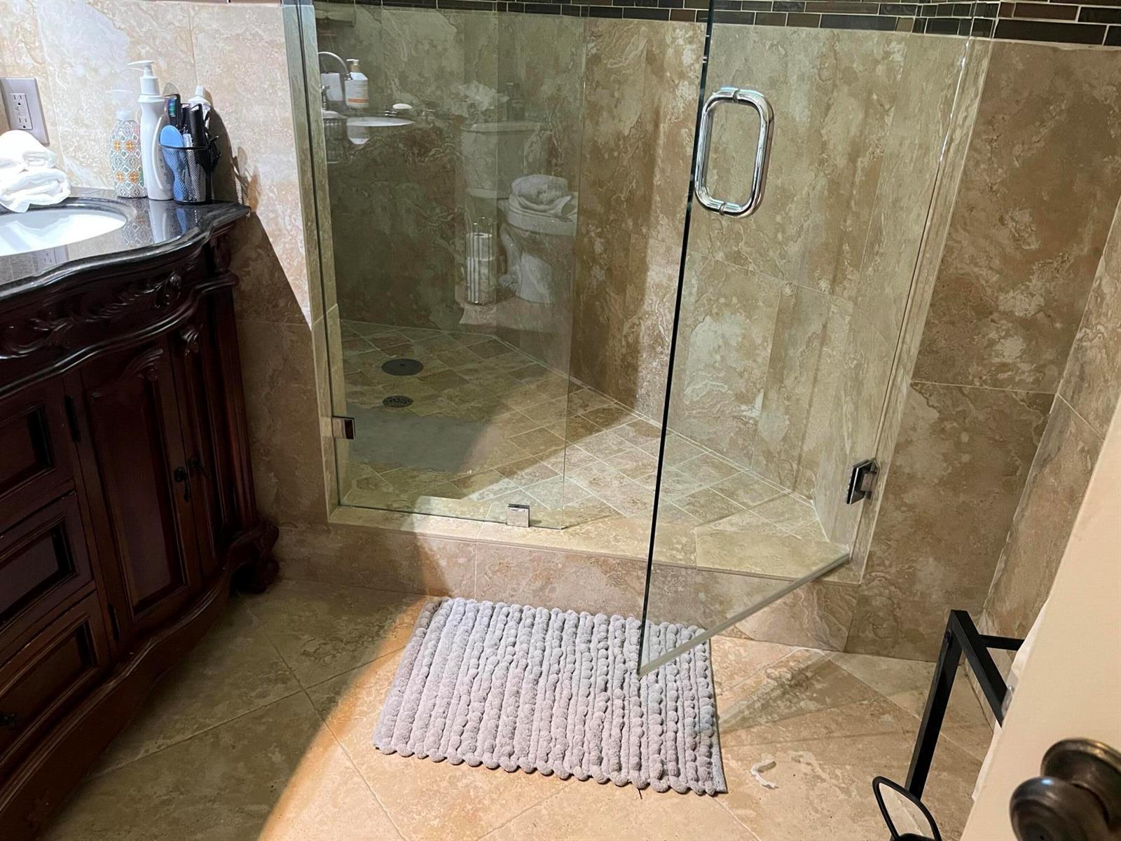 A bathroom features a glass-enclosed walk-in shower with tan stone tile and a dark vanity — 6549 Via Regina # 6549, Boca Raton FL 33433, BOCA RATON, FL