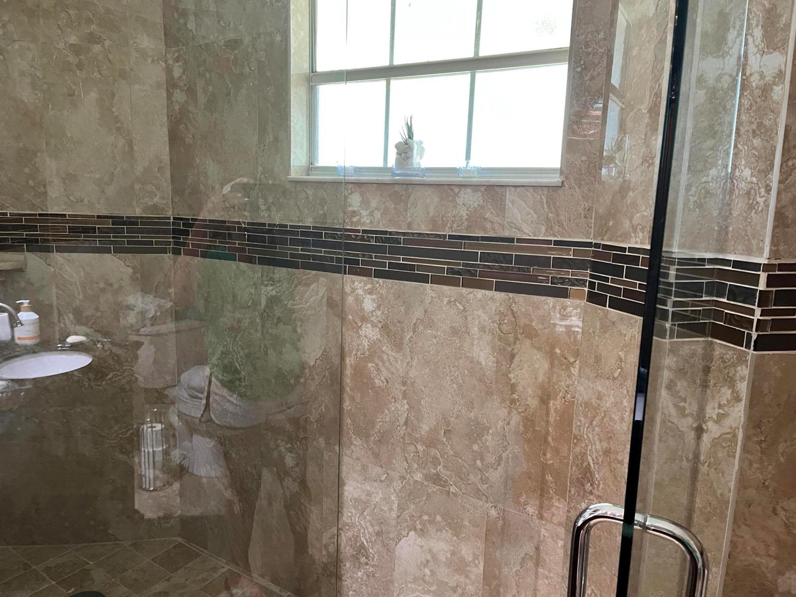 A glass-enclosed shower features tan stone wall tiles with a horizontal dark brown accent border — 6549 Via Regina # 6549, Boca Raton FL 33433, BOCA RATON, FL