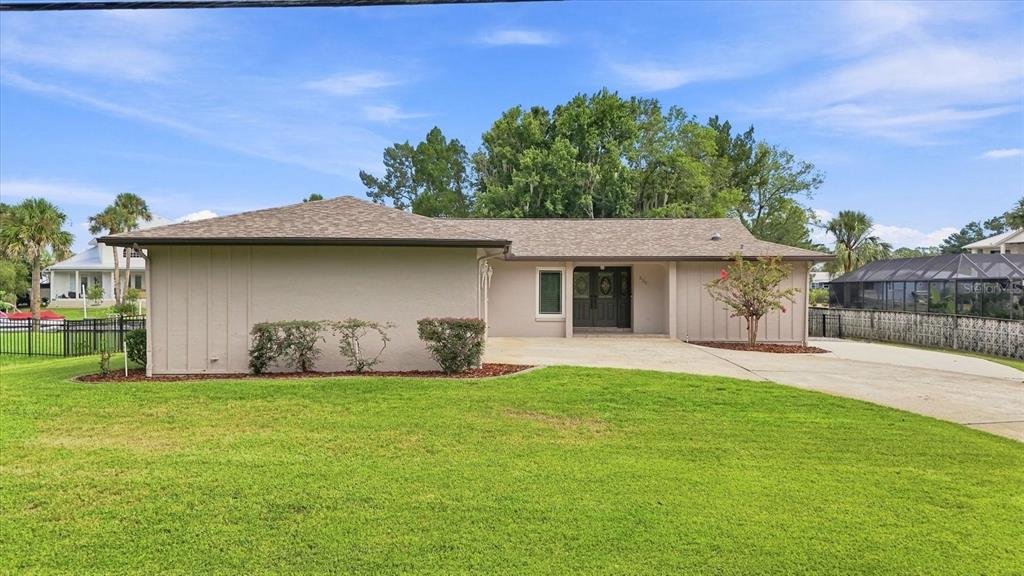 A single-story house with a beige exterior, a concrete driveway, and a large front lawn — 220 SE KINGS BAY DRIVE, CRYSTAL RIVER, FL