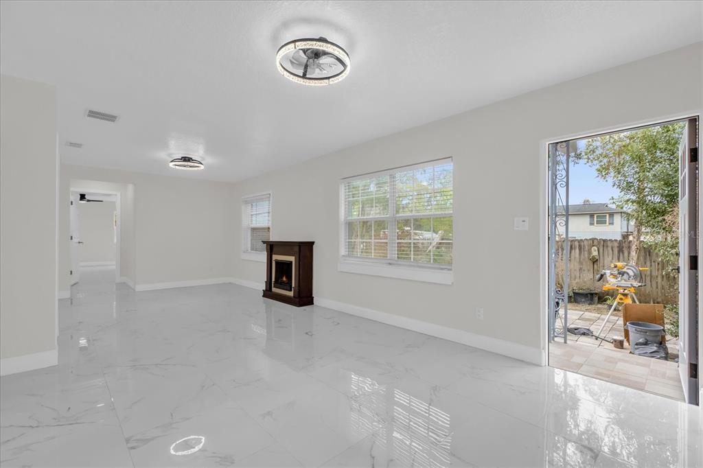 A bright room with white marble-look tile floors, a fireplace, and an open exterior door — 7506 MOTT AVENUE, ORLANDO, FL