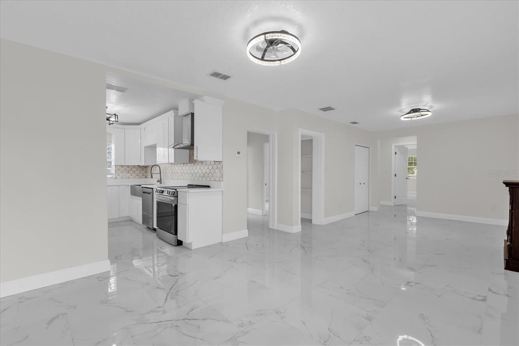 A bright, open-concept kitchen and living area featuring white cabinets and polished marble-look flooring — 7506 MOTT AVENUE, ORLANDO, FL