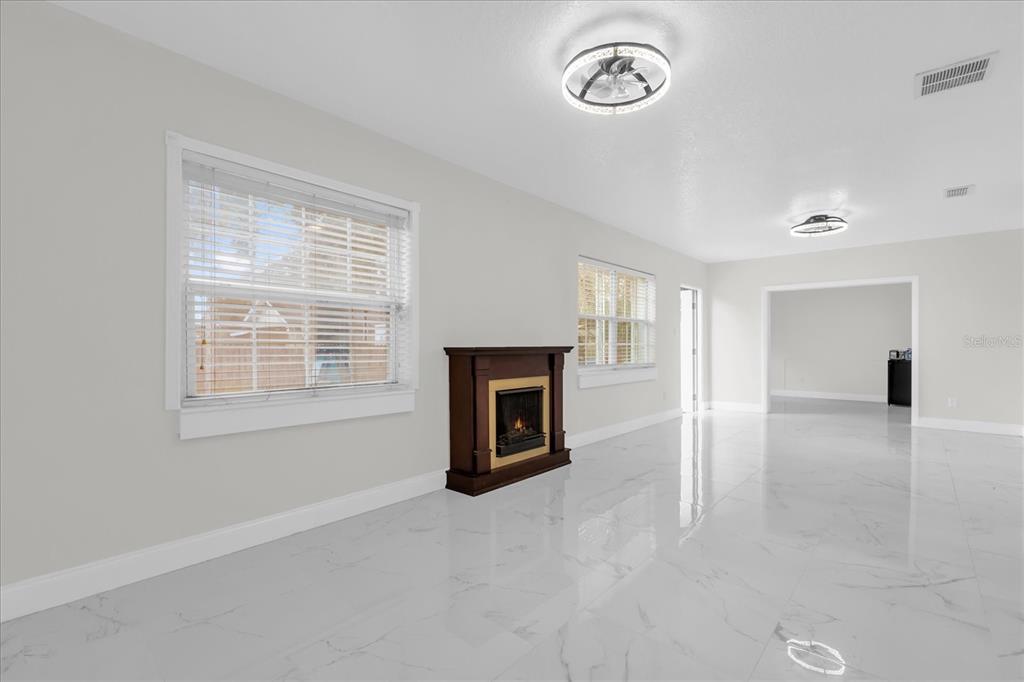 A bright living room features white walls, marble-look tile flooring, and a freestanding electric fireplace — 7506 MOTT AVENUE, ORLANDO, FL