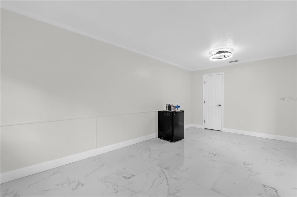 A room with white walls, white marble-look tile flooring, and a small black refrigerator — 7506 MOTT AVENUE, ORLANDO, FL