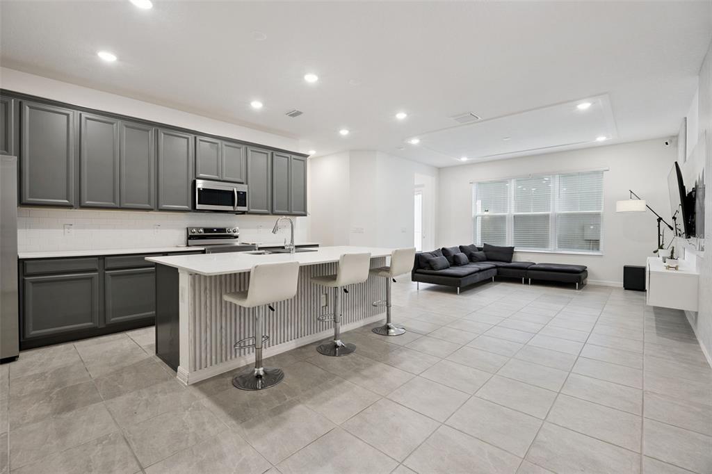 A modern open-concept kitchen with gray cabinets and a white island faces a living area — 7007 TWILIGHT BAY DRIVE, WINTER GARDEN, FL