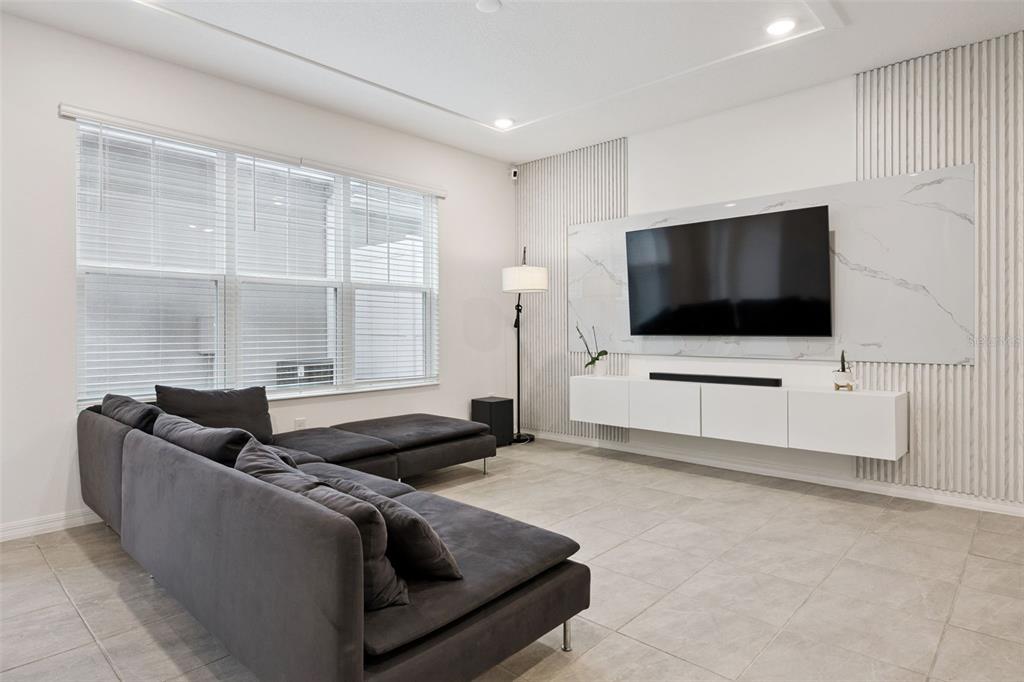 A living room features a dark sectional sofa, a wall-mounted TV, and vertical slat paneling — 7007 TWILIGHT BAY DRIVE, WINTER GARDEN, FL