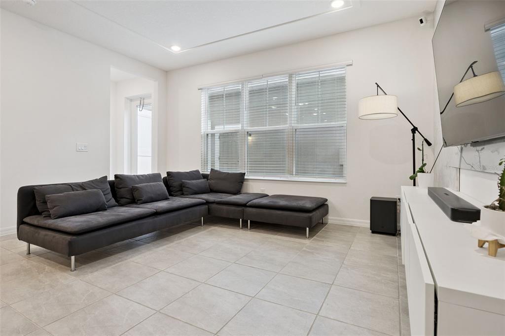 A living room features a large gray sectional sofa, tile flooring, and a wall-mounted television — 7007 TWILIGHT BAY DRIVE, WINTER GARDEN, FL