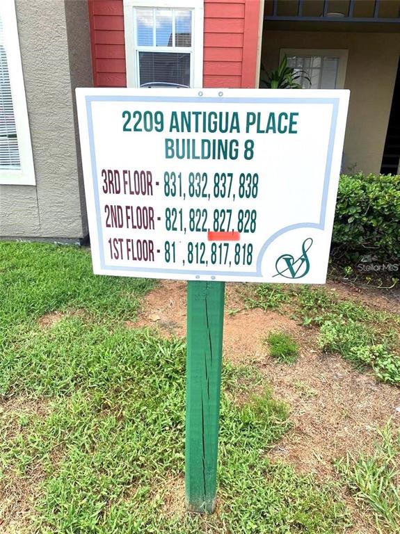 A sign on a green post lists apartment numbers for three floors of a building — 2209 ANTIGUA PLACE UNIT 827, KISSIMMEE, FL
