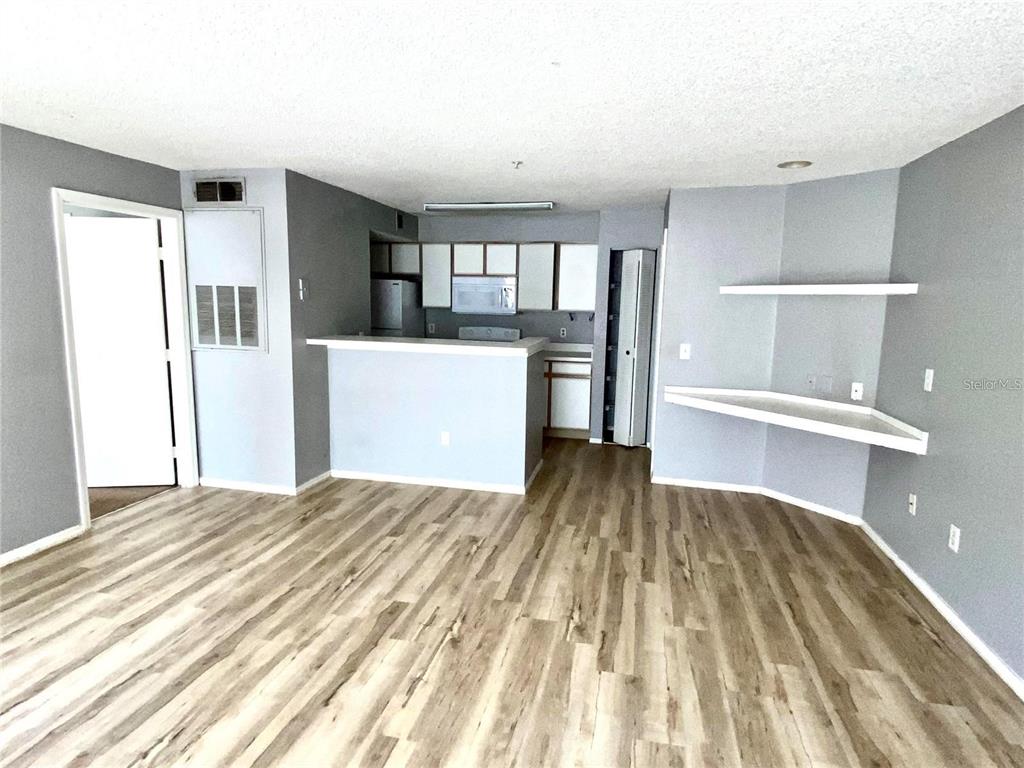 An open-concept living area features wood-look flooring, a kitchen with a breakfast bar, and shelving — 2209 ANTIGUA PLACE UNIT 827, KISSIMMEE, FL