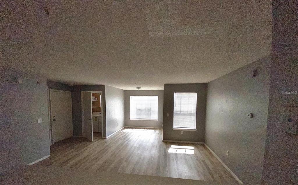 An empty living area features light-colored wood-look flooring, gray walls, and two windows with blinds — 2209 ANTIGUA PLACE UNIT 827, KISSIMMEE, FL