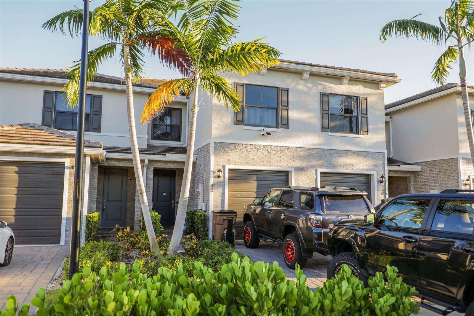 A two-story townhouse exterior with a paved driveway, two parked SUVs, and palm trees — 148 SE 5th Court, Deerfield Beach FL 33441, DEERFIELD BEACH, FL