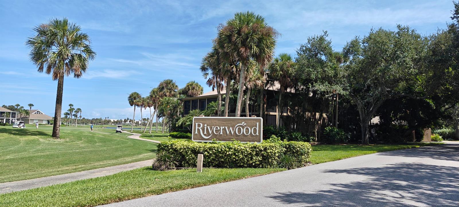 A sign for Riverwood stands in front of a golf course with palm trees and buildings — 233 NE Edgewater Drive # 203, Stuart FL 34996, STUART, FL