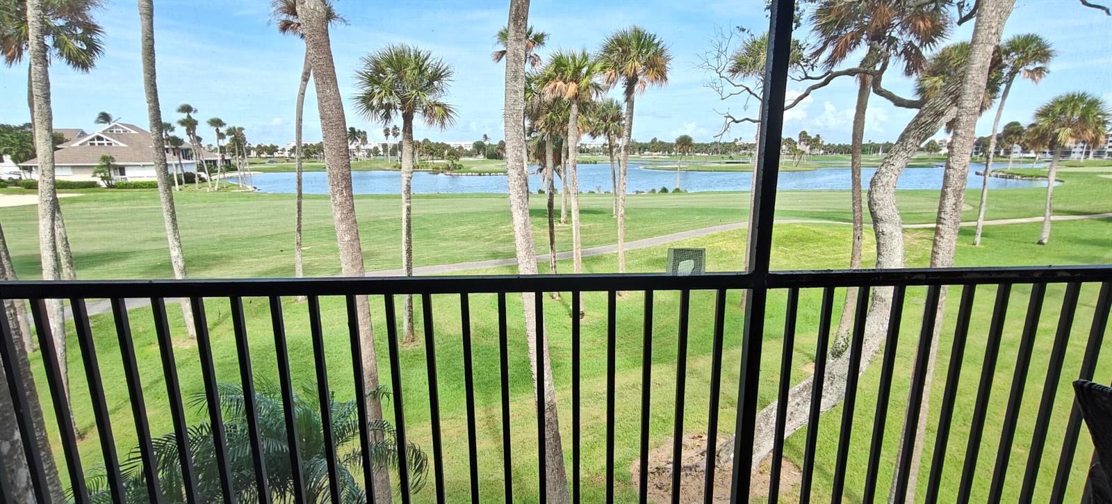 A view of a golf course and lake from a screened-in balcony with palm trees — 233 NE Edgewater Drive # 203, Stuart FL 34996, STUART, FL