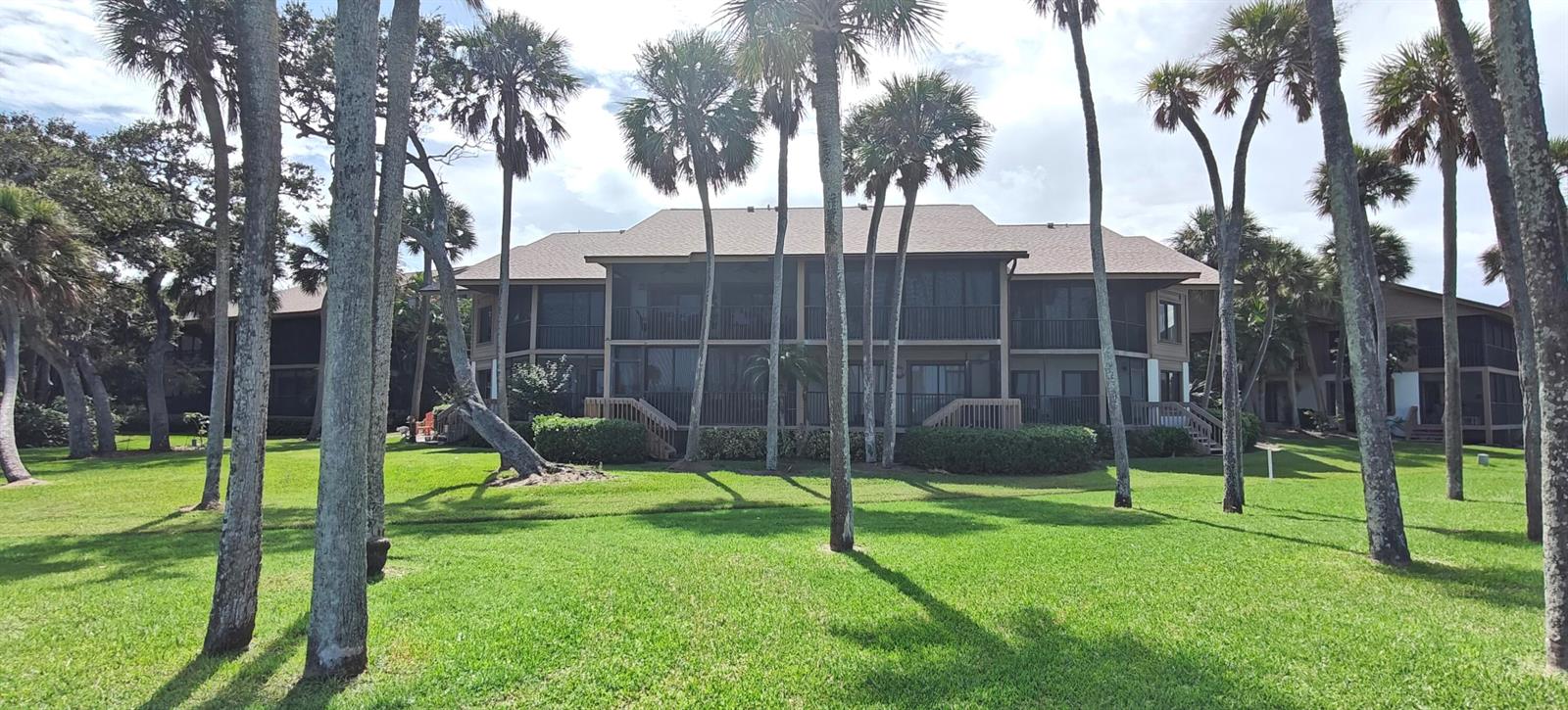 A multi-story apartment building with screened balconies surrounded by palm trees and a grassy lawn — 233 NE Edgewater Drive # 203, Stuart FL 34996, STUART, FL