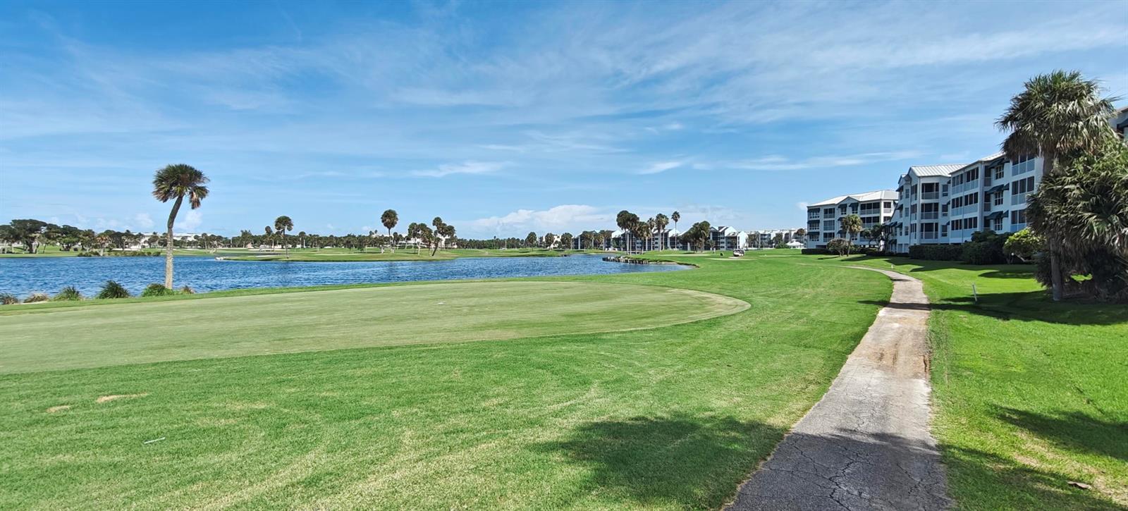 A golf course green sits beside a lake with residential buildings in the background — 233 NE Edgewater Drive # 203, Stuart FL 34996, STUART, FL