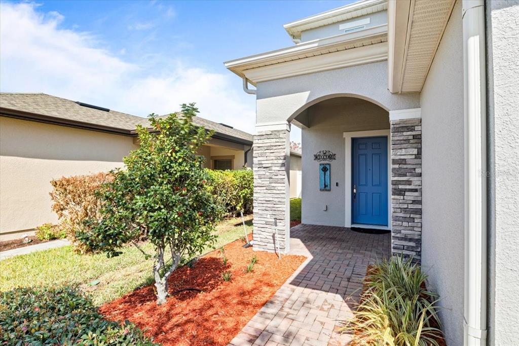 A blue front door is set within a stone-accented entryway with a brick paver walkway — 2642 FLICKER COVE, SANFORD, FL