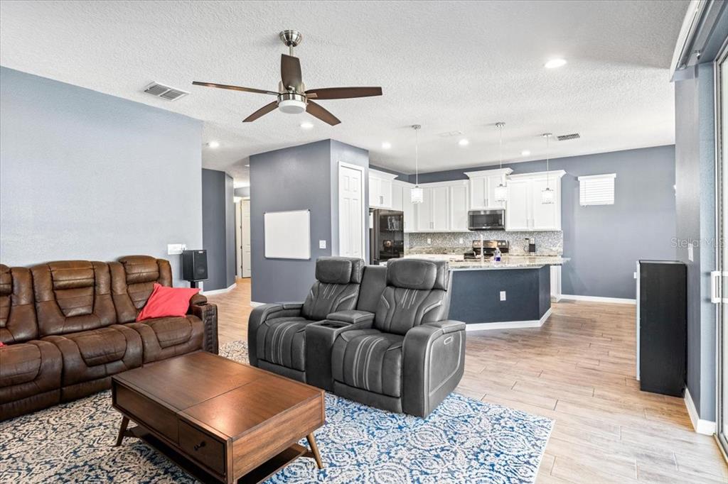 A living room with brown and gray sofas opens into a kitchen with white cabinets — 2642 FLICKER COVE, SANFORD, FL