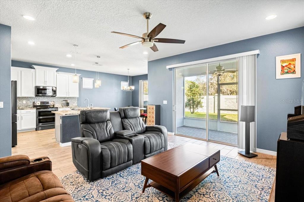 A living room with a grey recliner, coffee table, and open kitchen with white cabinets — 2642 FLICKER COVE, SANFORD, FL