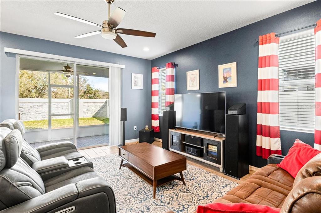 A living room features dark blue walls, a ceiling fan, a television, and sliding glass doors — 2642 FLICKER COVE, SANFORD, FL