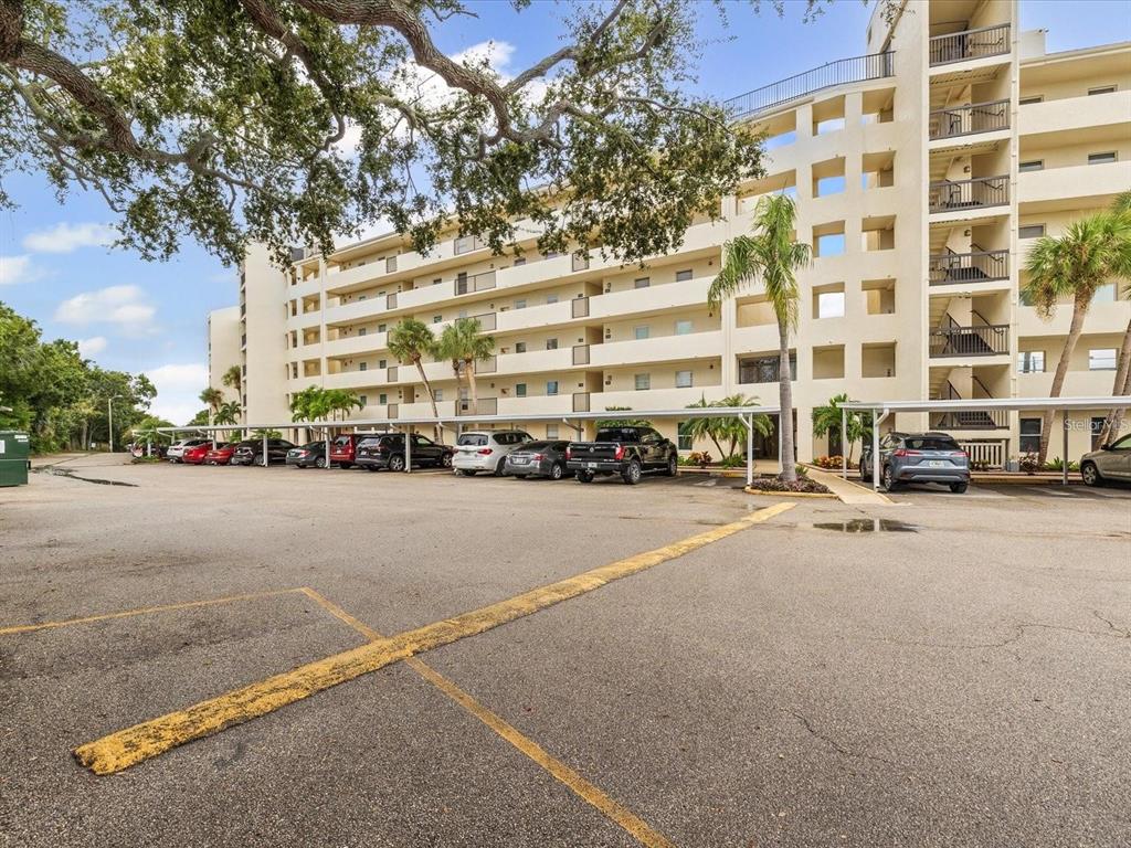 A multi-story apartment building with a covered parking lot and several parked cars — 225 COUNTRY CLUB DRIVE UNIT 1604, LARGO, FL