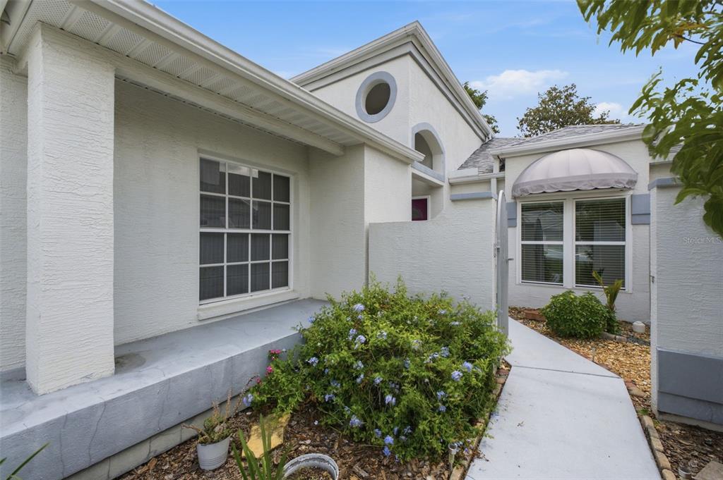 The exterior of a white stucco house features a walkway, a garden, and arched windows — 10428 CASA GRANDE CIRCLE, SPRING HILL, FL