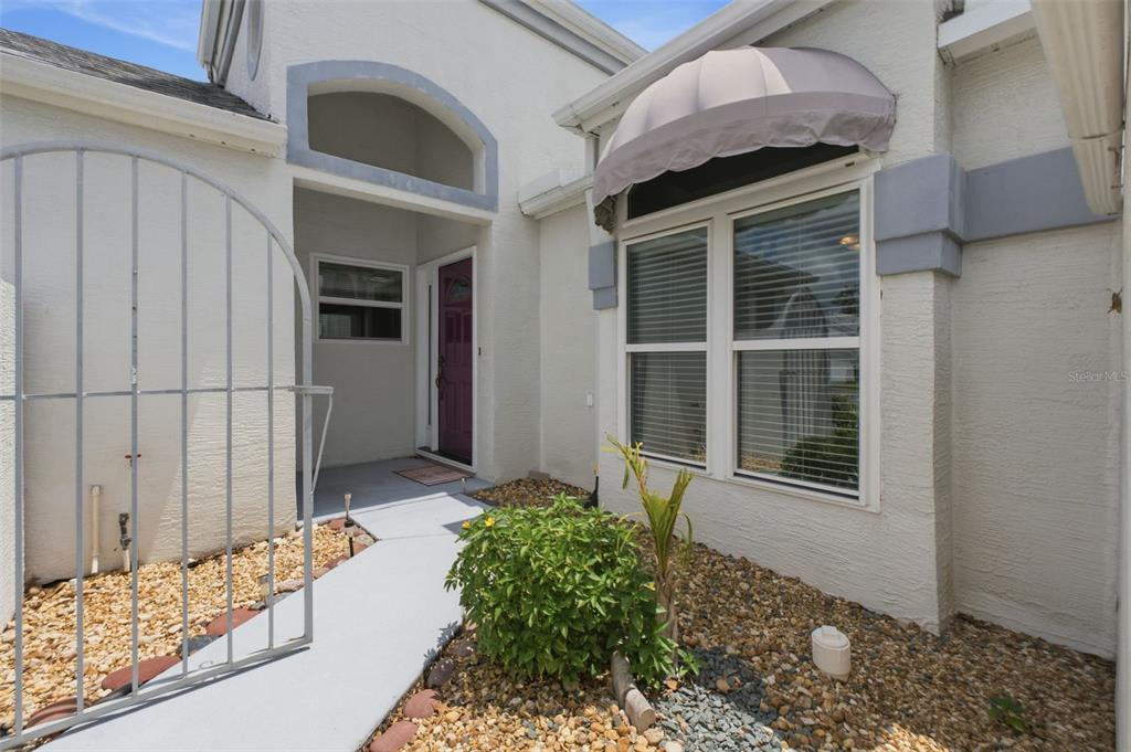 A white stucco house exterior features a purple front door, a metal gate, and awning — 10428 CASA GRANDE CIRCLE, SPRING HILL, FL