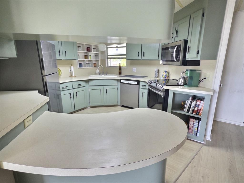 A kitchen features light green cabinets, stainless steel appliances, and a curved peninsula countertop — 46 PALM FOREST DRIVE, LARGO, FL