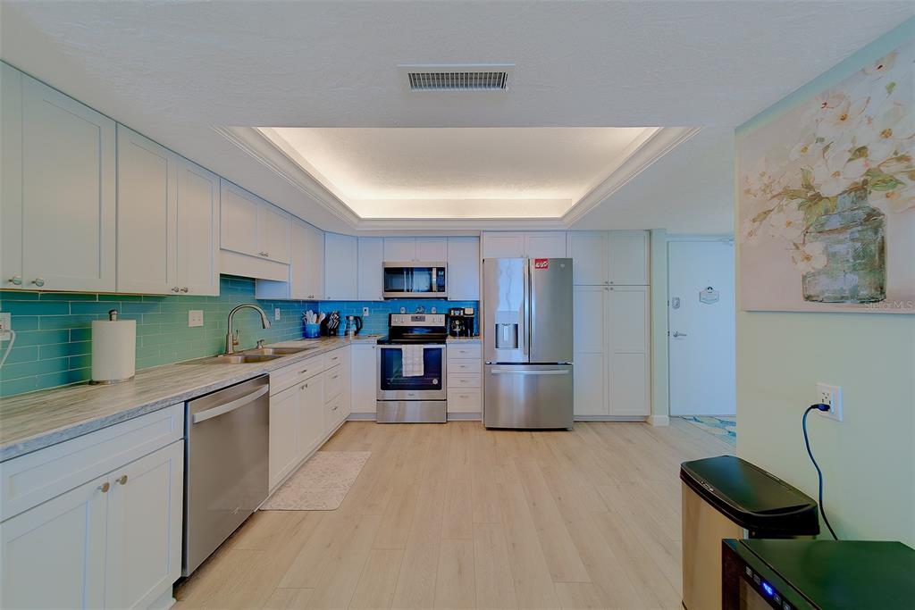 A bright kitchen features white cabinets, stainless steel appliances, and a turquoise subway tile backsplash — 17920 GULF BOULEVARD UNIT 1205, REDINGTON SHORES, FL