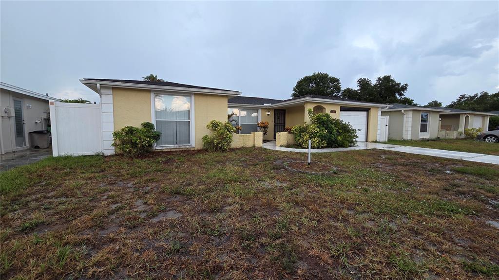 A single-story yellow house with a white garage and a patchy grass front yard — 7340 BRENTWOOD DRIVE, PORT RICHEY, FL