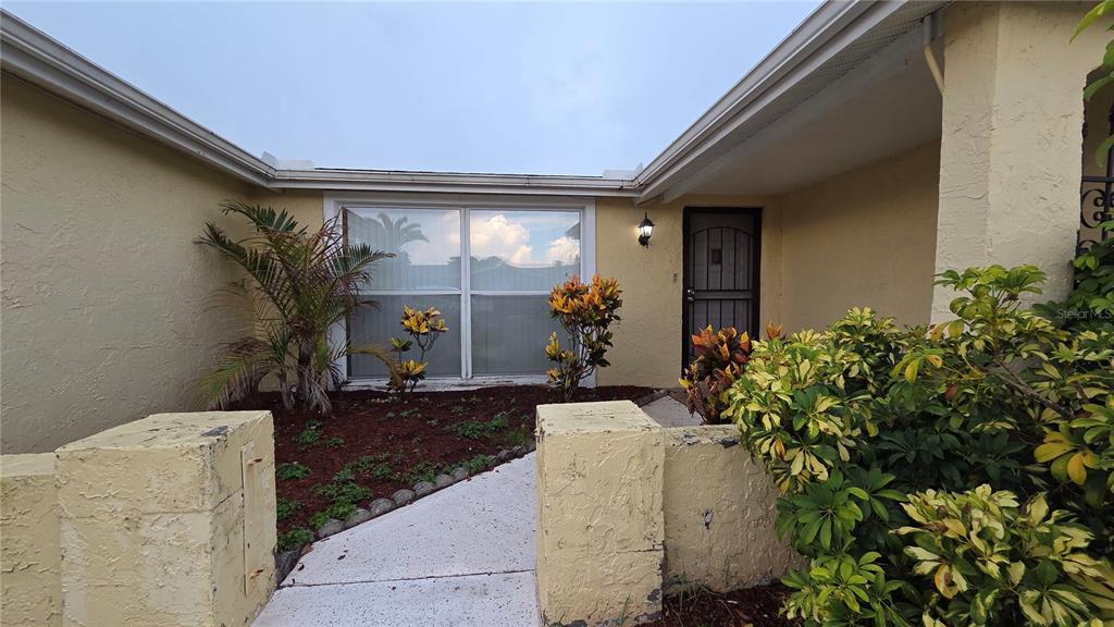A concrete walkway leads to the front entrance of a yellow house with landscaping — 7340 BRENTWOOD DRIVE, PORT RICHEY, FL