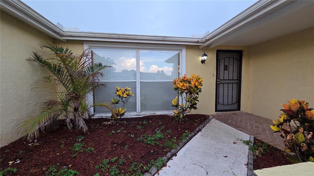 The exterior of a home features a front entrance, a large window, and landscaped beds — 7340 BRENTWOOD DRIVE, PORT RICHEY, FL