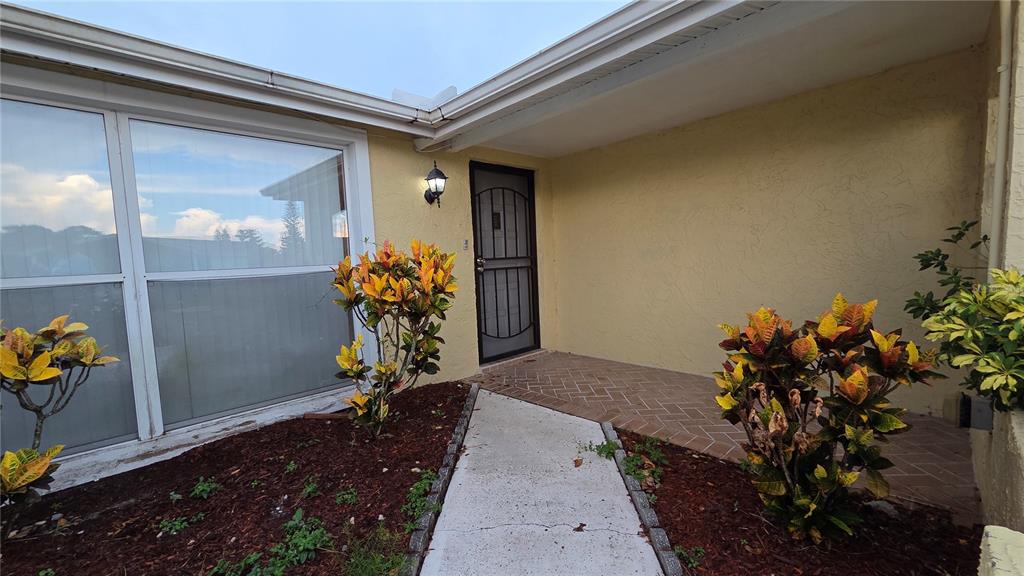 A concrete walkway leads to a front door with a screen door under a porch — 7340 BRENTWOOD DRIVE, PORT RICHEY, FL