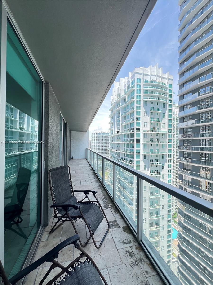 A balcony with stone tile flooring, two folding chairs, and a glass railing overlooking city buildings — 55 SE 6th St # 3305, Miami FL 33131, MIAMI, FL