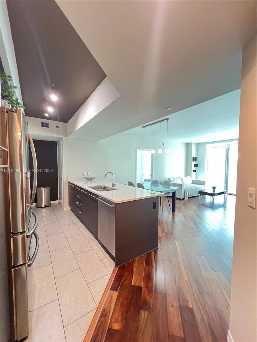 A modern kitchen with dark cabinetry and a white island opens into a living area — 55 SE 6th St # 3305, Miami FL 33131, MIAMI, FL