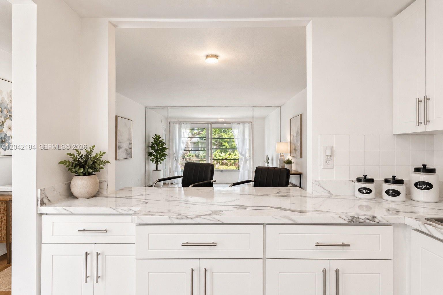 A white kitchen with marble countertops overlooks a living area with large sliding glass doors — 7605 NW 5th Pl # 103, Margate FL 33063, MARGATE, FL
