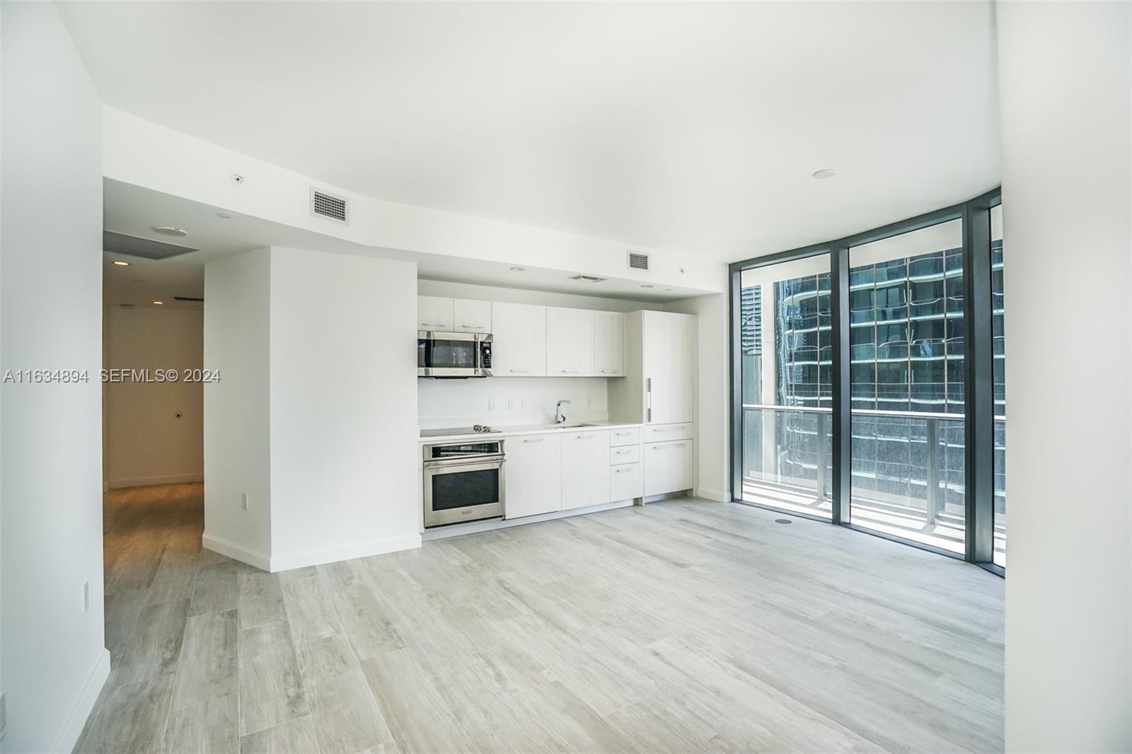 A modern kitchen with white cabinetry and stainless steel appliances opens to a living area — 55 SW 9th ST # 2108, Miami FL 33130, MIAMI, FL
