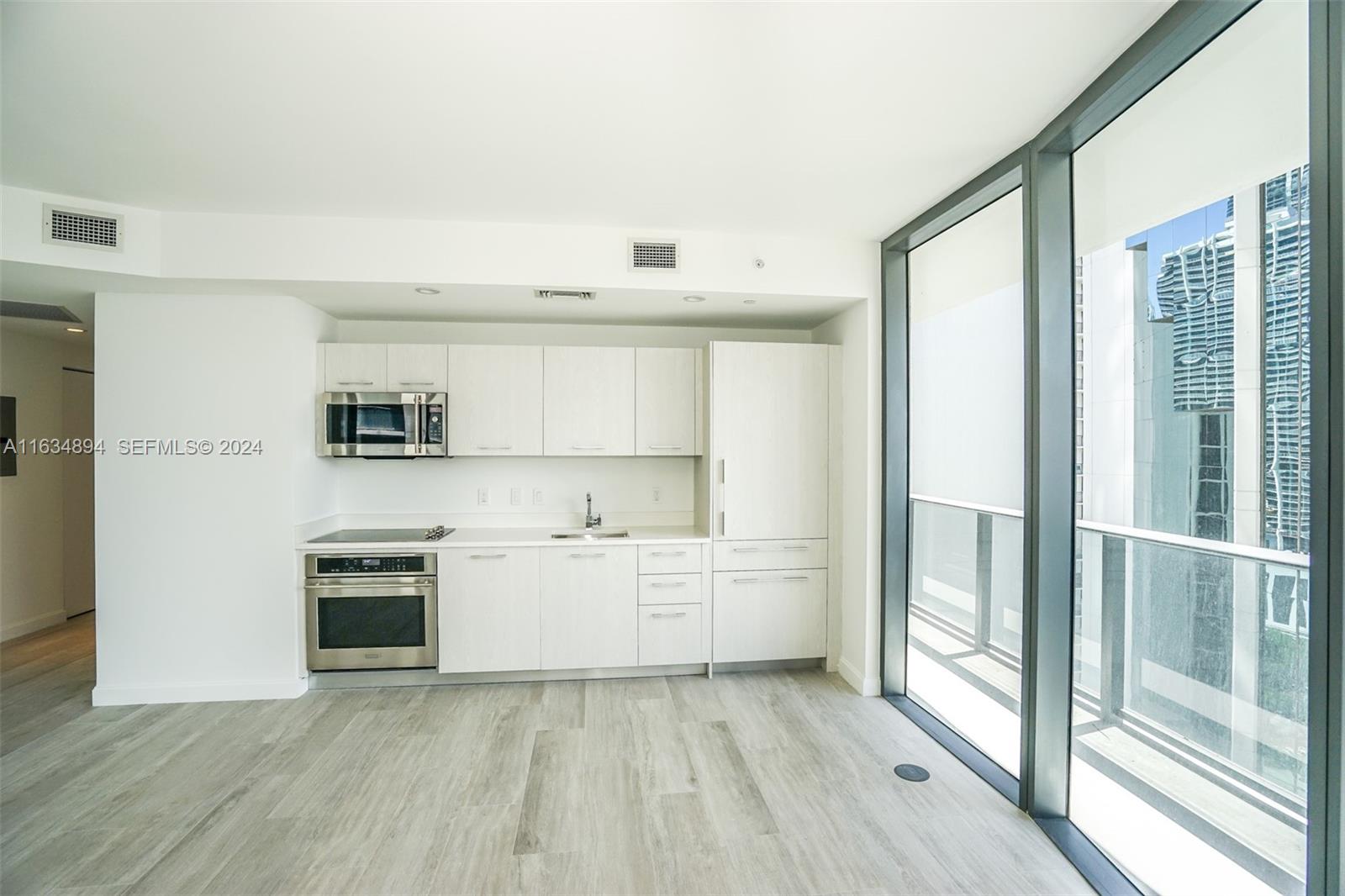 A modern kitchen features white cabinetry, stainless steel appliances, and floor-to-ceiling windows overlooking a balcony — 55 SW 9th ST # 2108, Miami FL 33130, MIAMI, FL