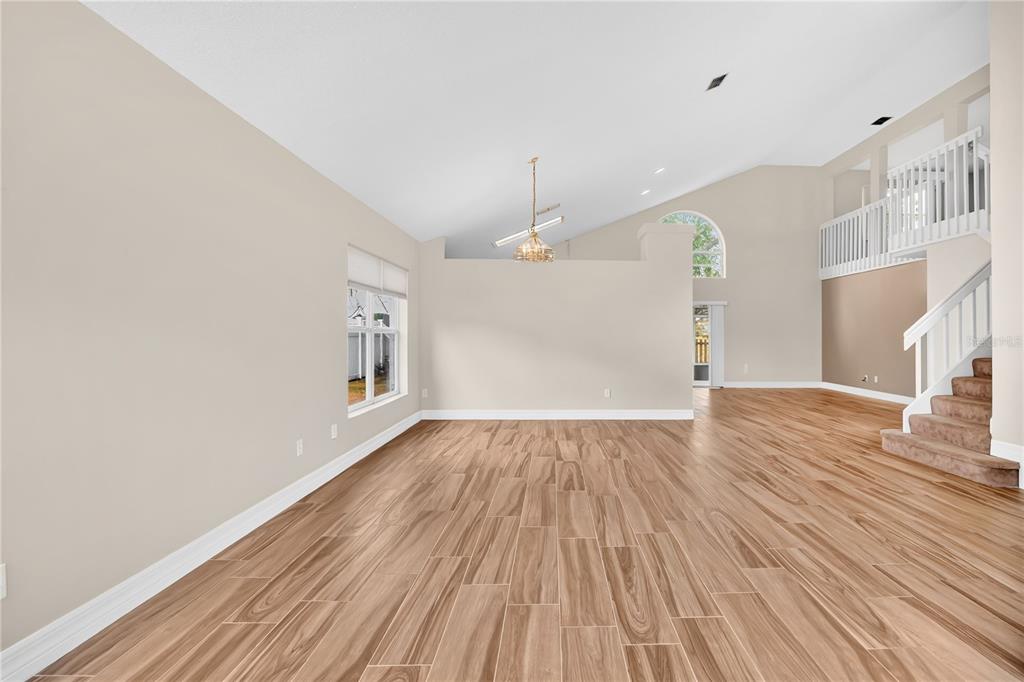 An empty living room features wood-look tile flooring, a vaulted ceiling, and a carpeted staircase — 13538 FORDWELL DRIVE, ORLANDO, FL